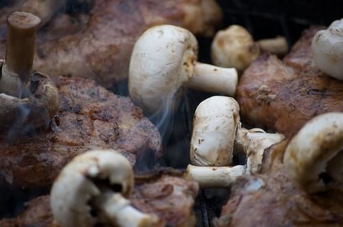 Closeup of mushrooms and steak on a grill with light smoke rising