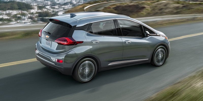 Grey Chevrolet Bolt EV driving on a mountain road over a city