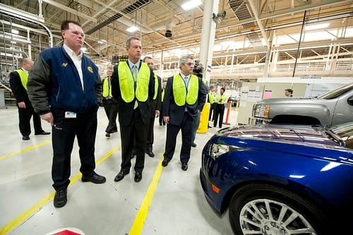 Men in suits tour GM factory and look at vehicles made with genuine parts